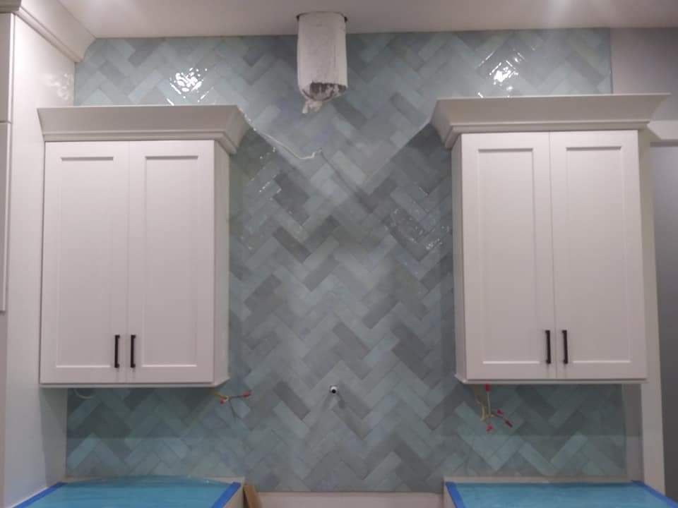Herringbone tile backsplash between white shaker cabinets